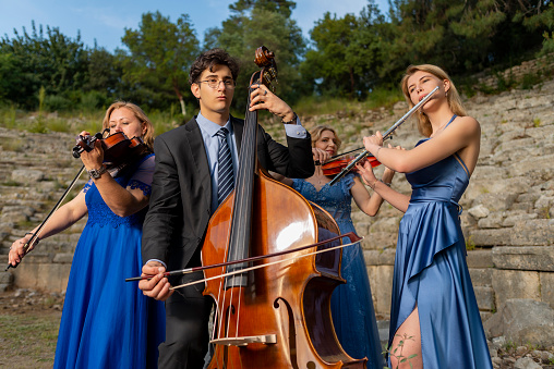 Three musicians in blue dress and one musician in black suit in ancient theater. Music group playing violin, flute and double bass. Album cover. Antalya, Kemer, Phaselis ancient city.