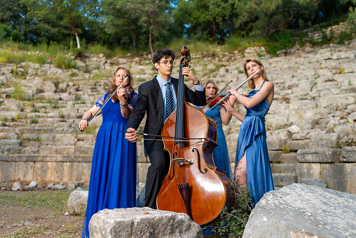 Three musicians in blue dress and one musician in black suit in ancient theater. Music group playing violin, flute and double bass. Album cover. Antalya, Kemer, Phaselis ancient city.
