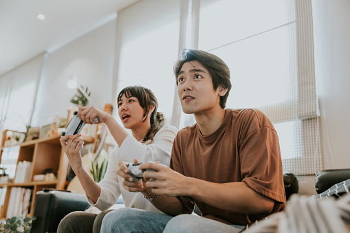 Asian girl holding joystick while playing video game with her boyfriend and feeling excited when she almost win this game.