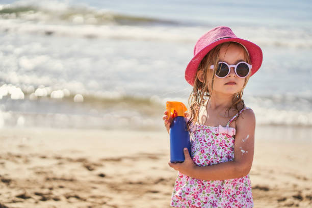 portrait of a girl with a bottle of sunscreen on the beach stock photo
