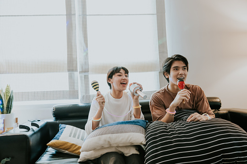 Happy two asian sibling enjoy singing karaoke at home together, favorite hobby.