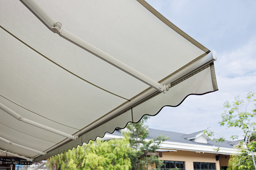 white fabric awning with the garden background. white canvas sun shading roof side view.