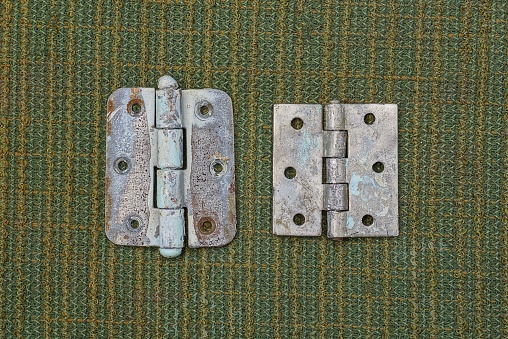 two old gray metal door hinges lie on a green cloth table