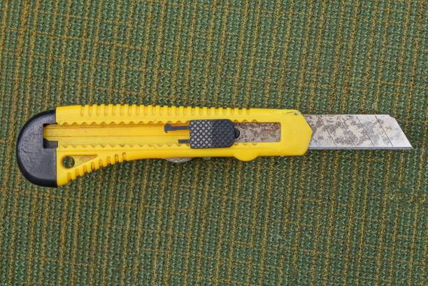 one yellow black stationery knife with a blade lies on a green table