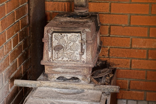 one gray old cast iron antique wood burning stove stands in a room against a red brick wall