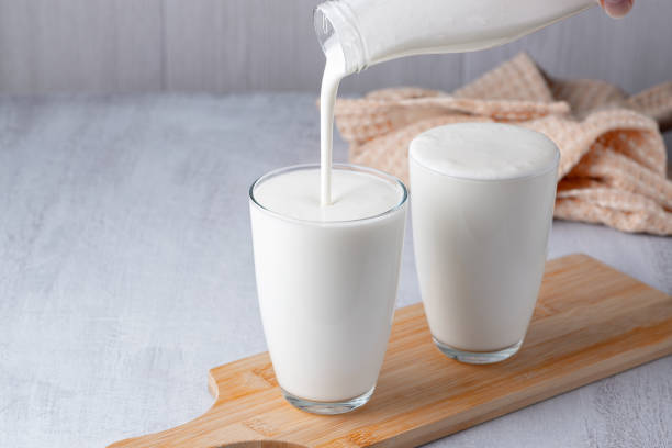 verser du kéfir maison, du babeurre ou du yogourt avec des probiotiques. yaourt s’écoulant d’une bouteille en verre sur fond clair. boisson laitière fermentée à froid probiotique. nourriture et boissons à la mode. espace de copie. - fungus science bottle glass photos et images de collection