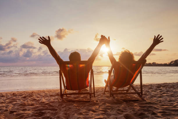 пляжный отдых, счастливая пара на пенсии, наслаждающаяся закатом у моря - retirement sun sunset senior adult стоковые фото и изображения
