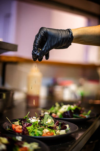 istock Cook's hand with black plastic glove dropping seeds on a salad in a restaurant kitchen. 1405469382