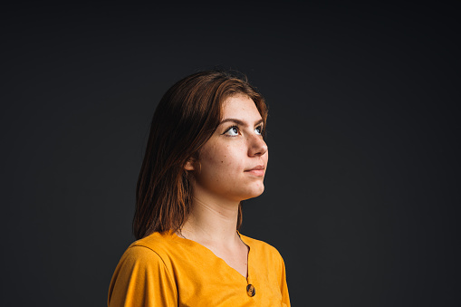Close up portrait of pretty confident thoughtful girl, holding hand near the face, looking seriously up, standing over grey background with copy space
