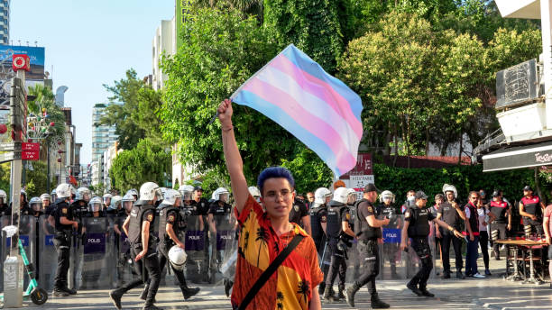 lgbtq-mitglied schwenkt flagge vor polizeikräften - pride lgbtqi veranstaltung stock-fotos und bilder