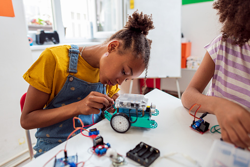 Side view of young  African girl programming electric toys and robots at classroom.