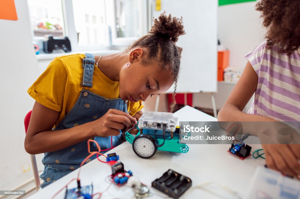 Focused girl on STEM class, making robots Side view of young  African girl programming electric toys and robots at classroom. Robotics Stock Photo