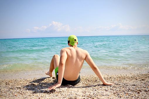 Teenage boy sitting near the sea with green bandana on his head