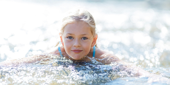 Little cute girl swims in the river, smiles. Happy childhood times in summer.