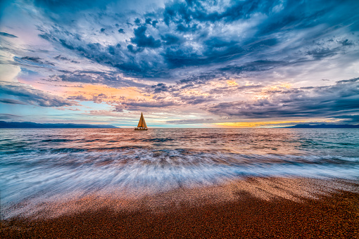 A Sailboat Sails Along The Ocean With A Colorful Cloudscape Overhead