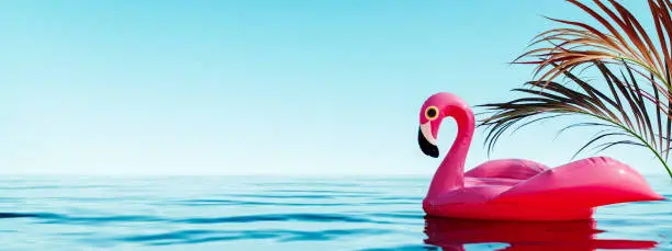 Photo of Pink flamingo inflatable in water with palm leaf decoration and blue sky background