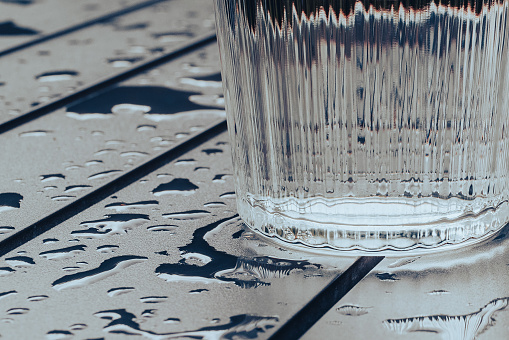 Close up of a fluted glass of water, resting on a metal garden table, wet after a rain storm.  Belfast, Northern Ireland.