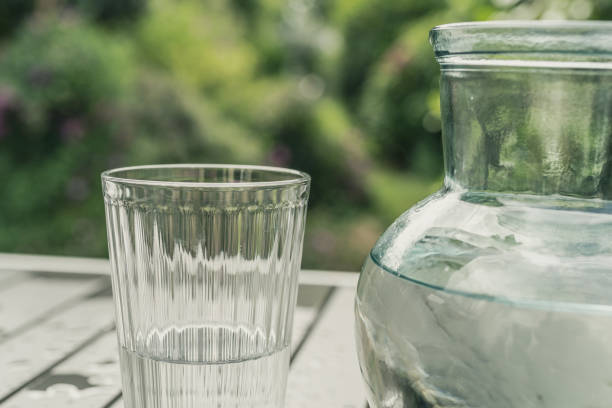 Glass of water, half empty, and a jug on a metal table stock photo