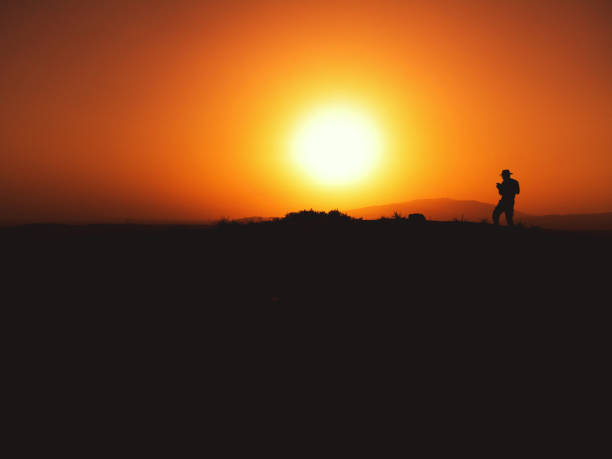 Silhouette of a man with fedora hat on sunset on a hill.