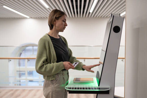 mujer de mediana edad registrando un libro en la biblioteca, utilizando un terminal de autoservicio - autoservicio fotografías e imágenes de stock