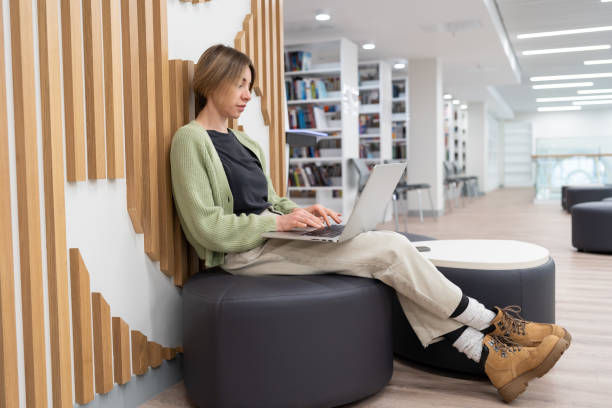 istock Focused middle-aged woman freelancer working on laptop computer in library, typing on keyboard 1405494149