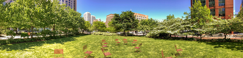 Red Chairs in the Rose Fitzgerald Kennedy Greenway's Wharf District Park. This park connects Faneuil Hall and the Financial District with Boston Harbor. Children playing in the Rings Fountain's vertical water jets as vendors sell their products in tents along the greenway.