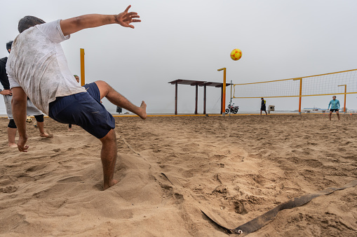 Back of a man practising ball kicking on the beach with a net of footvolley