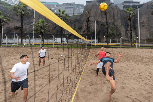Masculine team performing a training footvolley match on a beach