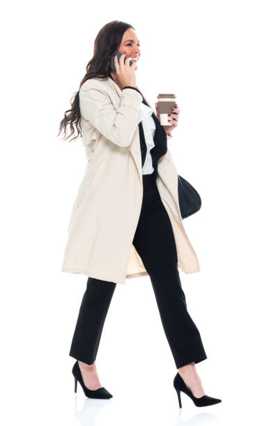 Caucasian young women manager walking in front of white background wearing businesswear and holding purse and using mobile phone stock photo