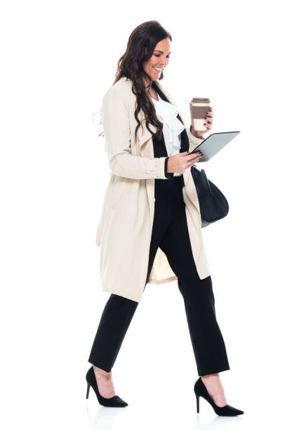 caucasian young women manager walking in front of white background wearing businesswear and holding purse and using touch screen - ações de bolsa imagens e fotografias de stock