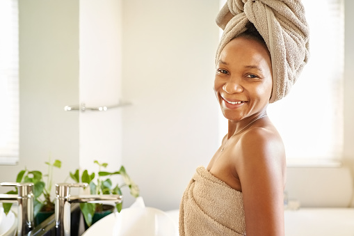 Portrait of a beautiful african woman wrapped in a towel standing in bathroom and looking at camera