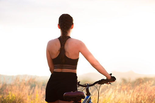 Woman with her mountain bike standing still enjoying the sunset landscape. Concept of healthy living, freedom and enjoying life.