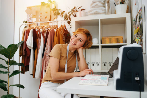 istock Charmingly smiling seamstress sitting behind her workdesk, working on laptop 1405516659