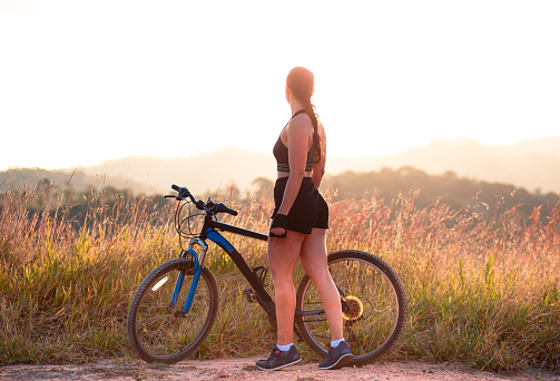 Woman with her mountain bike standing still enjoying the sunset landscape. Concept of healthy living, freedom and enjoying life.