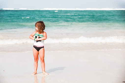 Happy little girl stands in shore water at Bavaro beach, Dominican Republic