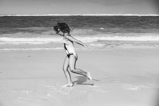 Little girl rins over shore water at the beach, black and white photo