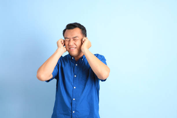 Middle Age Man The Asian middle aged man with blue shirt standing on the blue background. man closing ears photos stock pictures, royalty-free photos & images