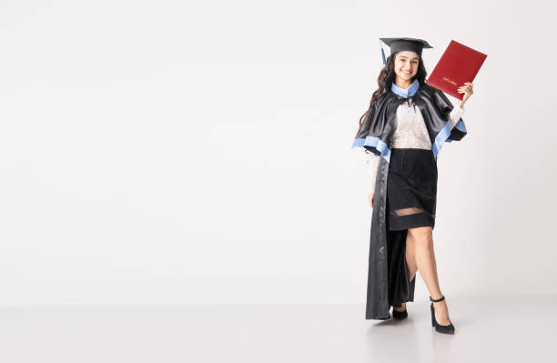 istock Woman student with diploma on white background with copy space. University graduate indian race woman wearing academic regalia and holding red diploma. 1405519906