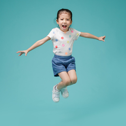 Playful energetic Asian little girl jumping in mid-air, empty space in studio shot isolated on colorful blue background