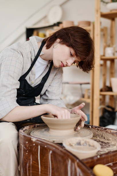 istock Young female pitcher bending over rotating pottery wheel during work 1405520285
