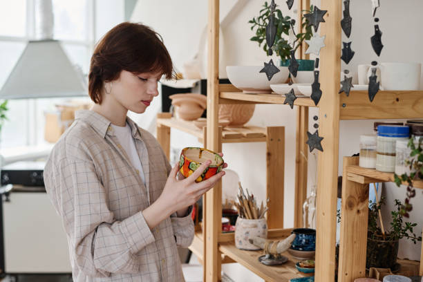 istock Young brunette woman choosing gift in earthenware shop while holding clay bowl 1405520339