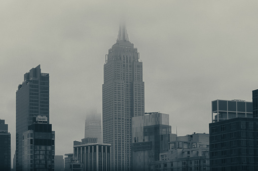 Editorial Use - A gray gloom covers Manhattan, with the Empire State Building centered here. The building, contrasting with its modern neighbors, metaphorically shows the long lasting power of classical sentiments by piercing through a blanket of fog.

Designed by architecture firm Shreve, Lamb & Harmon, the Empire State Building is a famous landmark which held the record for tallest building in the world for almost 40 years. 
  
Taken in March of 2022, 92 years since the first day of its construction.