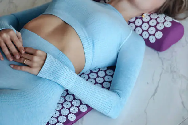 Acupressure mat massage therapy. Close-up young woman lying on orthopedic acupressure mat for self health massage in living room at home indoors. Person having alternative medicine relaxing treatment