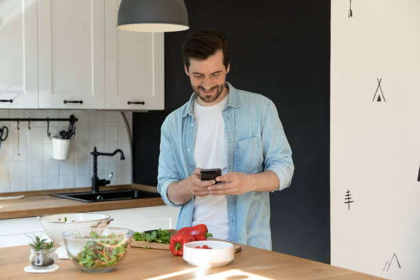 istock Man cooking in kitchen holding smartphone search online recipes 1405522768
