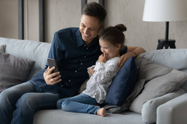istock Joyful young caring father and adorable small daughter using cellphone. 1405522945