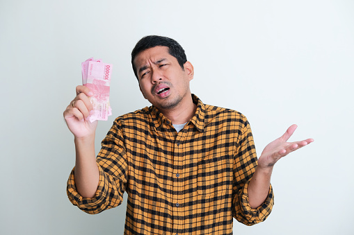 Adult Asian man showing sad expression when looking to paper money that he hold