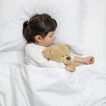 Child girl sleeping with teddy bear on the wooden bed in her bedroom, Happy asian child little girl with her teddy bear, family concept at home