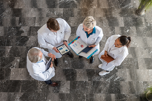 Team of doctors in lab coats working together having a discussion over research. The photo is shot from above.