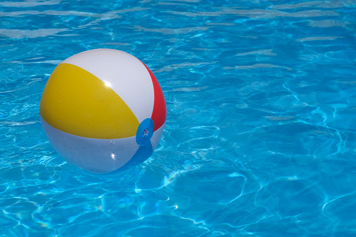 Colorful inflatable beach ball floating in beautiful shiny blue swimming pool in pure blue water. Family summer vacation, holiday and kids pool party. Healthy outdoor sport activity. Copy space