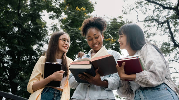 gruppe von multiethnischen diversity-schülerinnen, die ein buch lesen und hausaufgaben glücklich machen.gruppe von multiethnischen studentinnen, die ein buch lesen und hausaufgaben glücklich machen. bücherwurm-frauenerziehung. - multi ethnic group reading stock-fotos und bilder